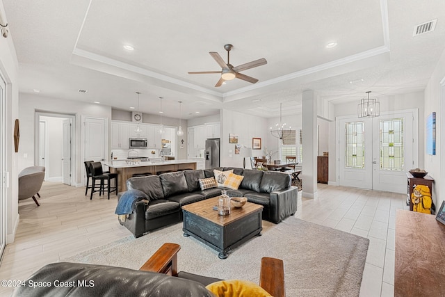 living room with crown molding, light hardwood / wood-style floors, ceiling fan with notable chandelier, and a raised ceiling