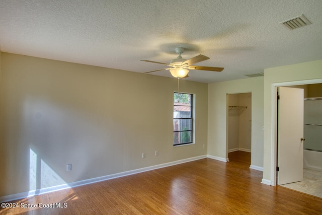 unfurnished bedroom featuring ceiling fan, a textured ceiling, a spacious closet, wood-type flooring, and a closet