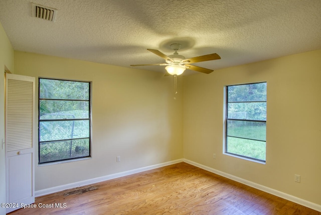 empty room with light hardwood / wood-style flooring, a textured ceiling, a wealth of natural light, and ceiling fan