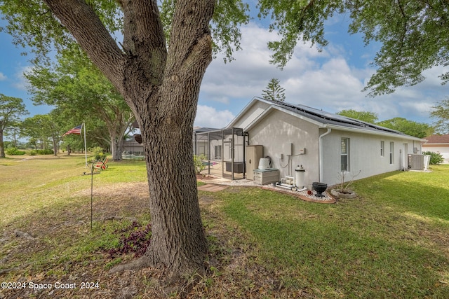 view of home's exterior with central air condition unit, glass enclosure, a lawn, and solar panels