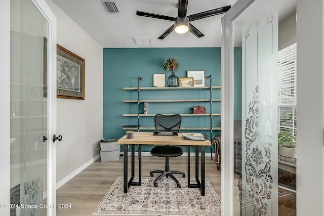 home office featuring ceiling fan, french doors, light hardwood / wood-style floors, and a textured ceiling