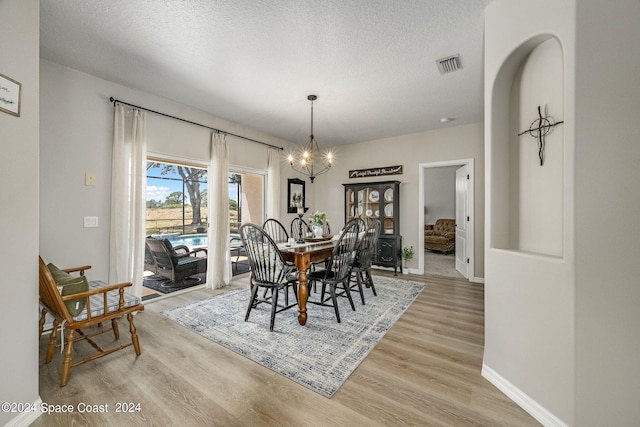 dining space featuring a notable chandelier, light wood-type flooring, and a textured ceiling