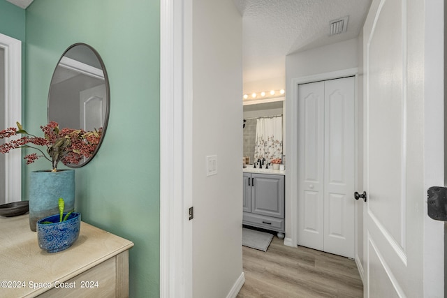 corridor with sink, light hardwood / wood-style flooring, and a textured ceiling