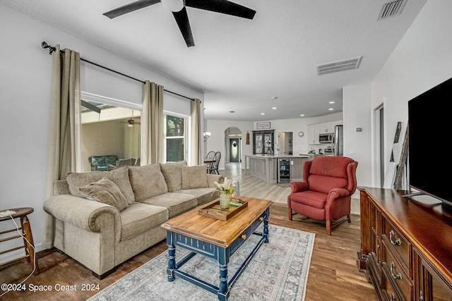 living room featuring ceiling fan, wine cooler, light wood-type flooring, and a textured ceiling