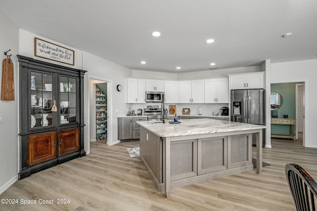 kitchen with a kitchen island with sink, appliances with stainless steel finishes, light wood-type flooring, and white cabinetry