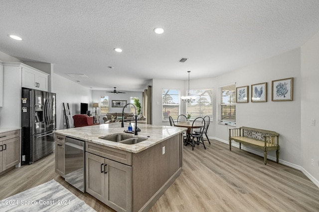 kitchen with light wood-type flooring, stainless steel appliances, sink, a center island with sink, and decorative light fixtures