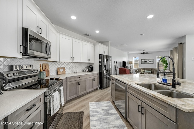 kitchen with light stone counters, white cabinets, sink, appliances with stainless steel finishes, and light hardwood / wood-style floors