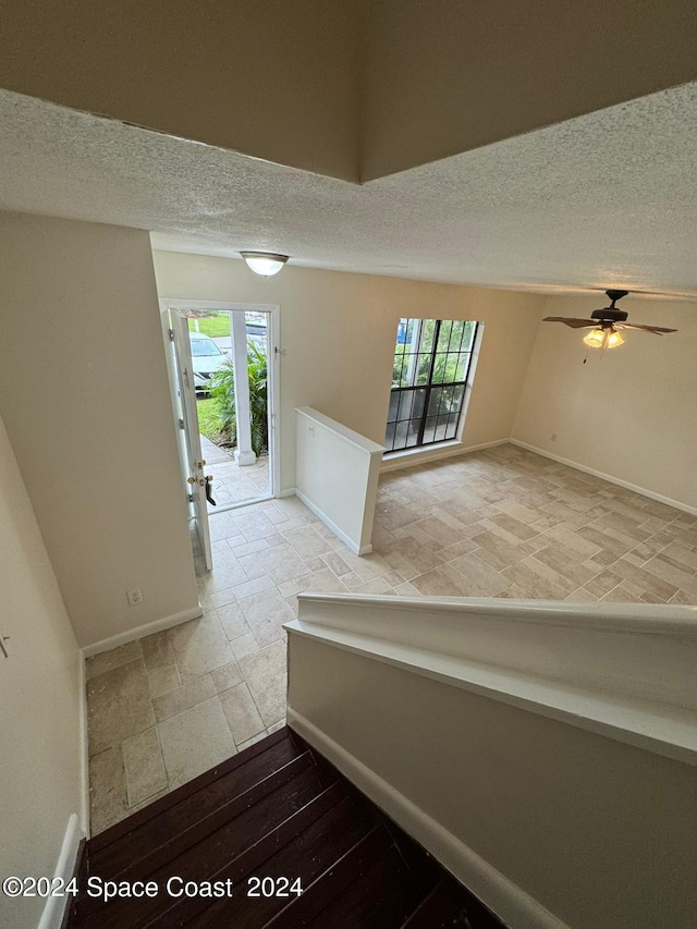 staircase with ceiling fan, a wealth of natural light, hardwood / wood-style floors, and a textured ceiling