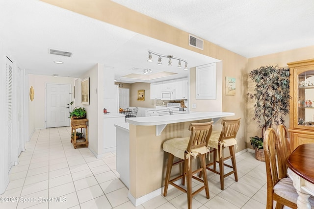 kitchen with a breakfast bar area, kitchen peninsula, white cabinets, a textured ceiling, and white appliances