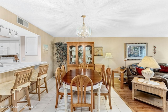 dining room featuring rail lighting, a notable chandelier, a textured ceiling, and light wood-type flooring