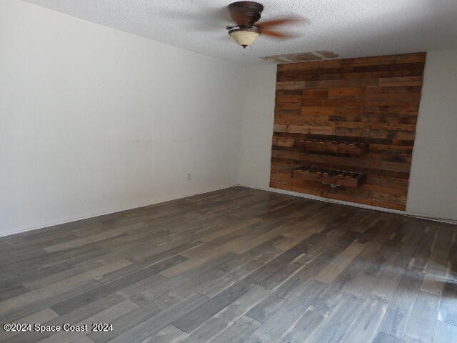 unfurnished room with ceiling fan, a textured ceiling, and dark wood-type flooring