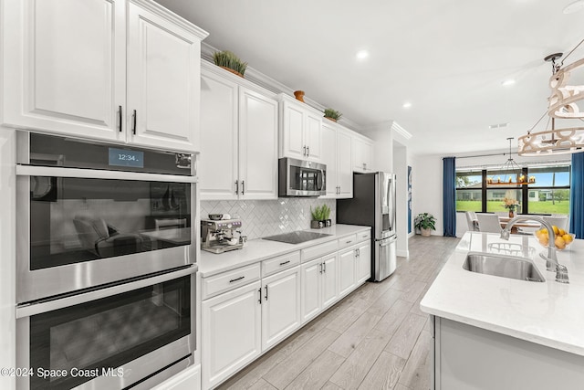 kitchen featuring light wood-type flooring, stainless steel appliances, sink, pendant lighting, and white cabinets