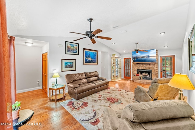 living room with vaulted ceiling, a fireplace, light hardwood / wood-style floors, and ceiling fan