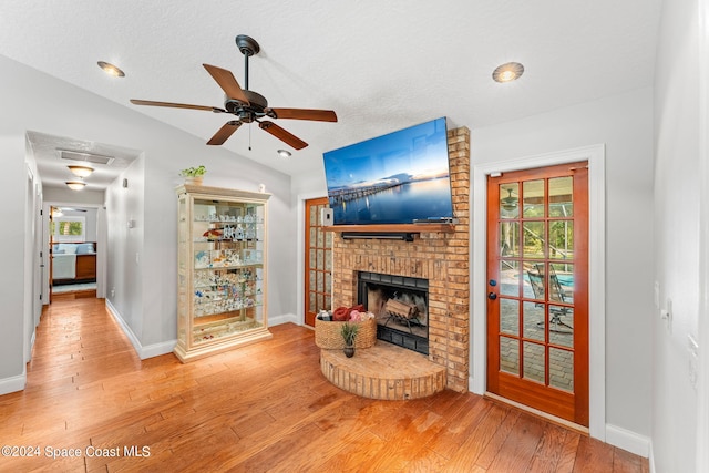 living room featuring vaulted ceiling, a brick fireplace, hardwood / wood-style flooring, and ceiling fan