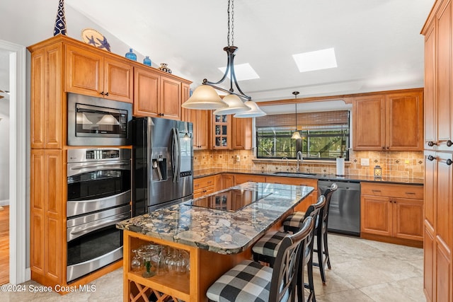 kitchen with dark stone counters, sink, a center island, a kitchen bar, and appliances with stainless steel finishes