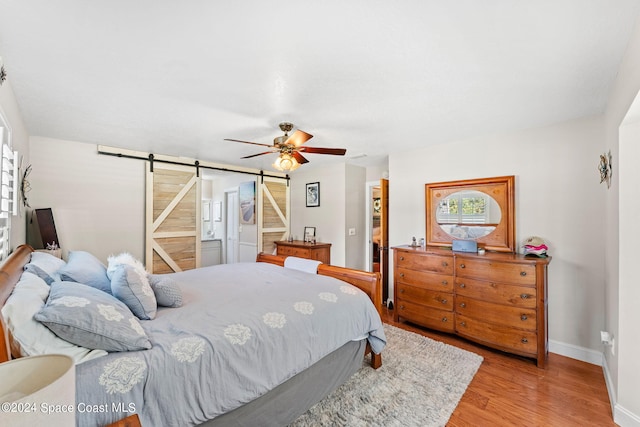 bedroom featuring a barn door, a spacious closet, a closet, ceiling fan, and light hardwood / wood-style flooring