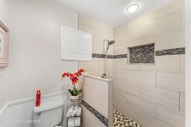 bathroom featuring a tile shower, a textured ceiling, and toilet