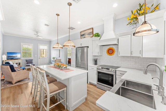 kitchen with light wood-type flooring, appliances with stainless steel finishes, premium range hood, and white cabinets