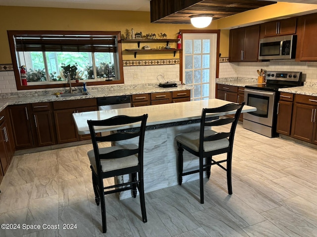 kitchen featuring decorative backsplash, light stone countertops, appliances with stainless steel finishes, and sink