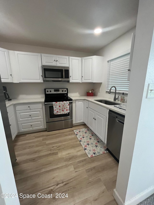 kitchen with stainless steel appliances, white cabinets, sink, and light wood-type flooring