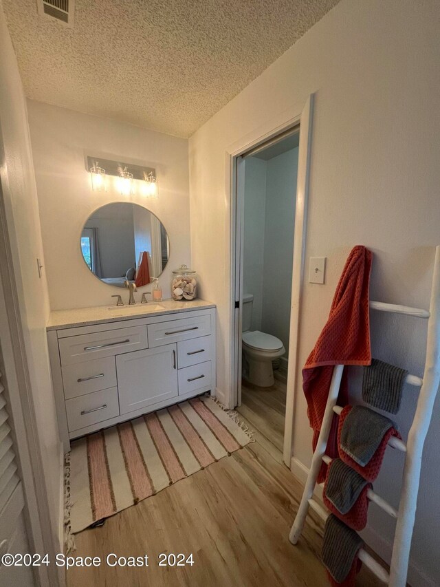 bathroom with wood-type flooring, vanity, toilet, and a textured ceiling