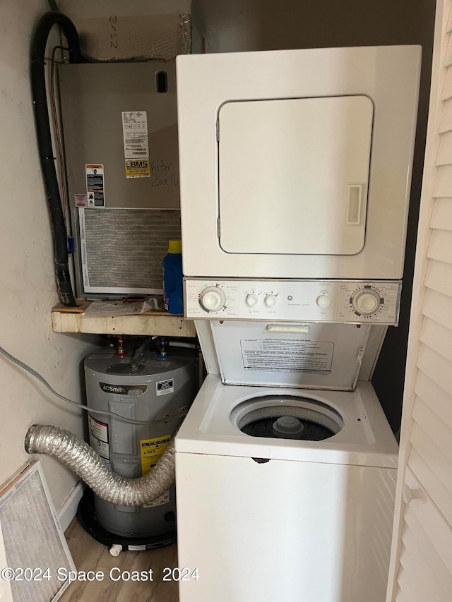 laundry room featuring wood-type flooring, water heater, and stacked washer / dryer