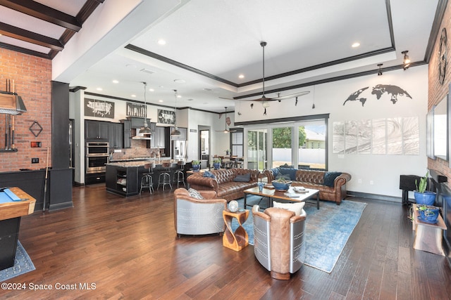 living room with a raised ceiling, dark wood-type flooring, beam ceiling, brick wall, and ornamental molding