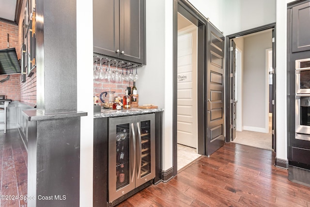 bar featuring brick wall, wine cooler, light stone countertops, and dark wood-type flooring