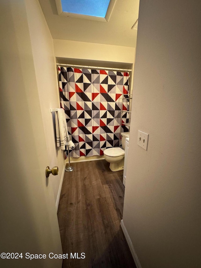 bathroom featuring toilet, a skylight, a shower with shower curtain, and hardwood / wood-style floors