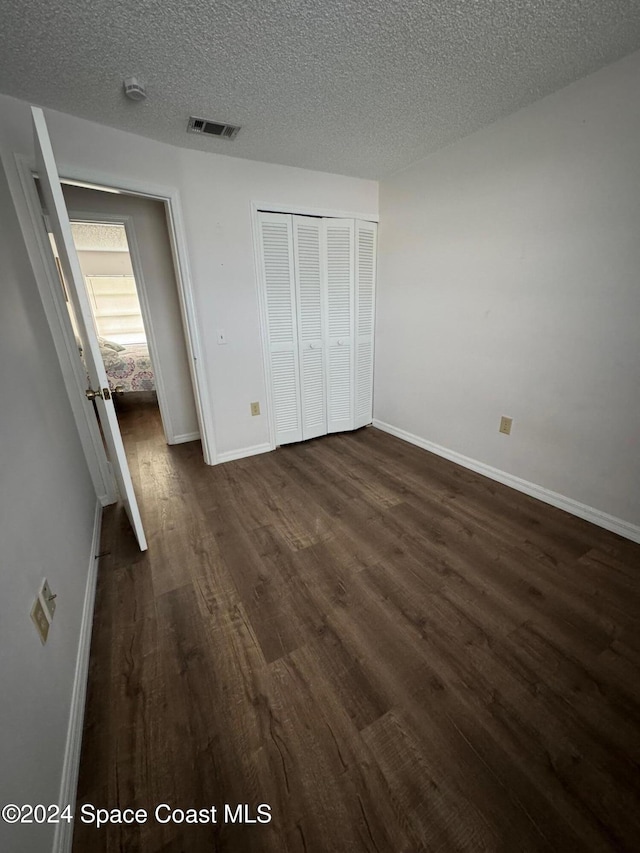 unfurnished bedroom with a textured ceiling, dark hardwood / wood-style floors, and a closet