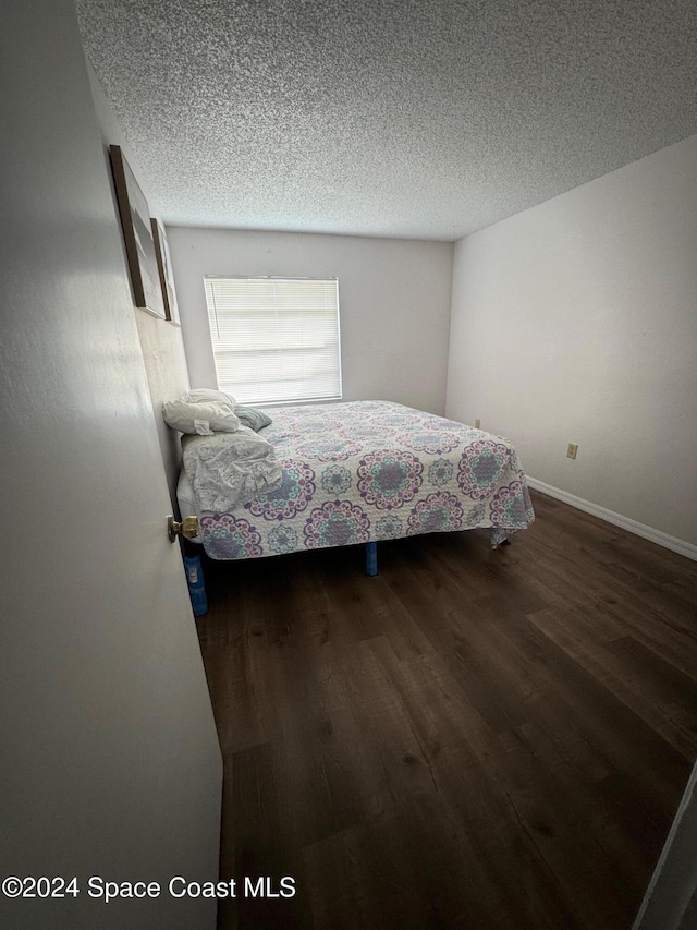 bedroom featuring a textured ceiling and dark hardwood / wood-style flooring