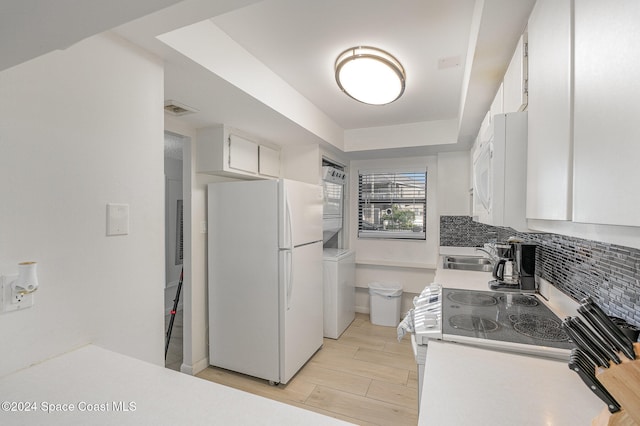 kitchen with white appliances, stacked washer / drying machine, tasteful backsplash, and white cabinets