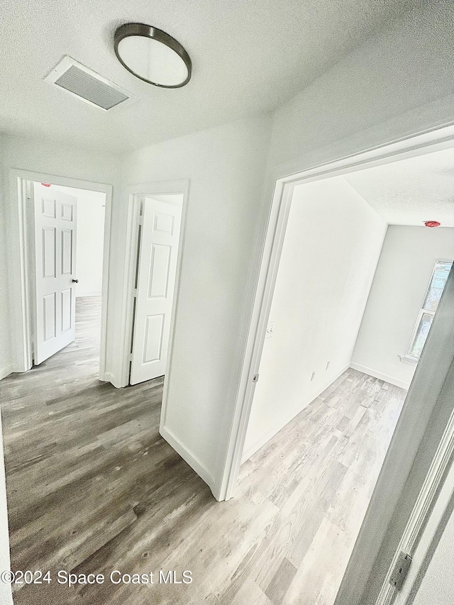 corridor featuring light wood-type flooring, a textured ceiling, and vaulted ceiling