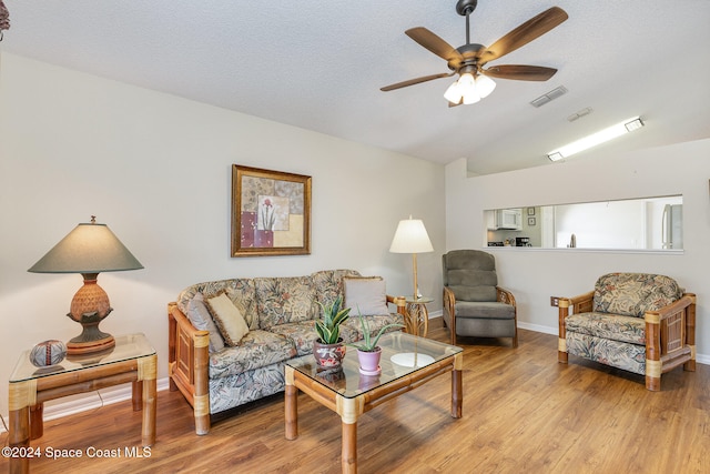 living room featuring vaulted ceiling, a textured ceiling, light hardwood / wood-style floors, and ceiling fan