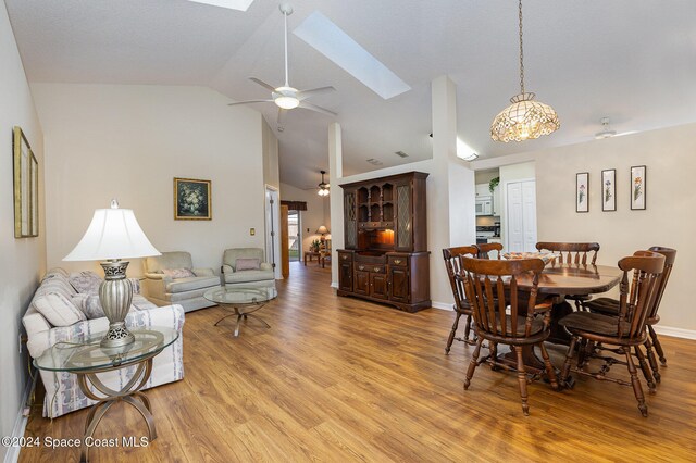 dining space featuring vaulted ceiling with skylight, light wood-type flooring, and ceiling fan