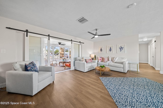 living room featuring ceiling fan, wood-type flooring, a barn door, and a textured ceiling