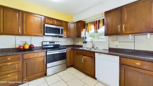 kitchen with decorative backsplash, dark stone counters, sink, stainless steel appliances, and light tile patterned floors