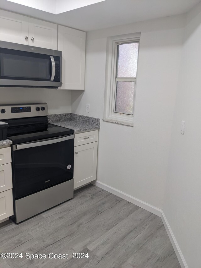 kitchen with appliances with stainless steel finishes, light stone counters, light wood-type flooring, and white cabinetry