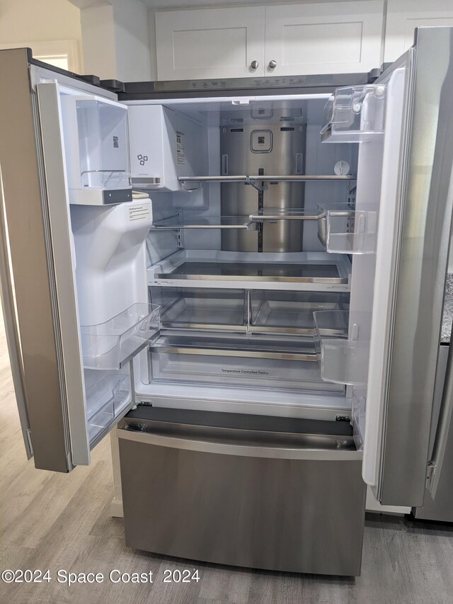 room details with white cabinets, hardwood / wood-style flooring, and stainless steel refrigerator