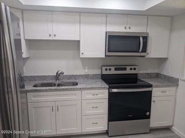 kitchen featuring appliances with stainless steel finishes, white cabinetry, light stone countertops, and sink