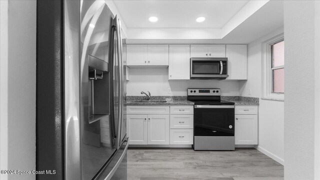 kitchen featuring appliances with stainless steel finishes, sink, light wood-type flooring, white cabinets, and dark stone countertops