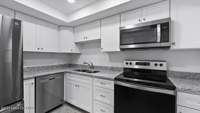 kitchen with white cabinets, stainless steel appliances, sink, and light stone counters