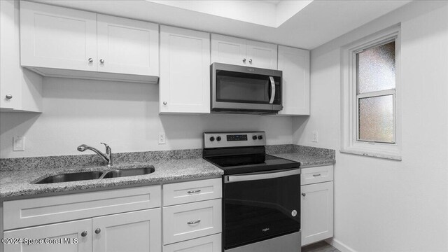 kitchen with appliances with stainless steel finishes, white cabinetry, light stone countertops, and sink