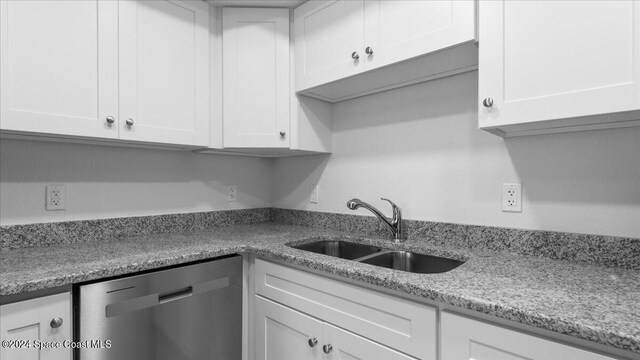 kitchen with stainless steel dishwasher, sink, white cabinets, and light stone counters