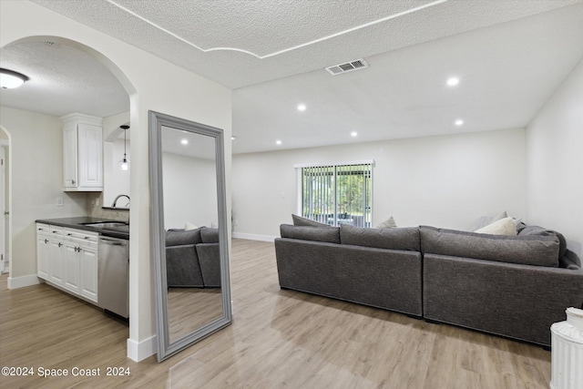 living room featuring sink, light wood-type flooring, and a textured ceiling