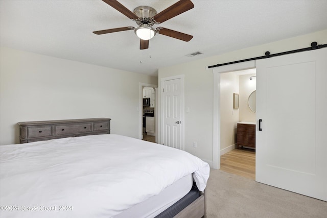 bedroom featuring ceiling fan, light colored carpet, a barn door, and ensuite bathroom