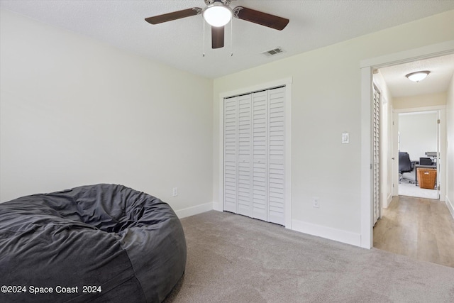 bedroom featuring light colored carpet, ceiling fan, a closet, and a textured ceiling