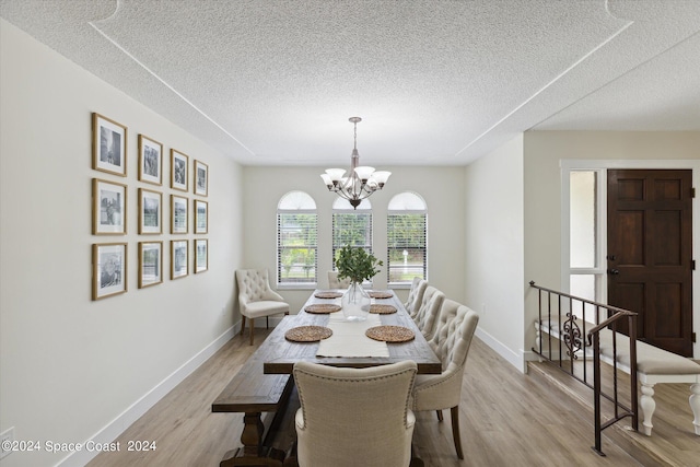 dining area featuring light wood-type flooring, a chandelier, and a textured ceiling