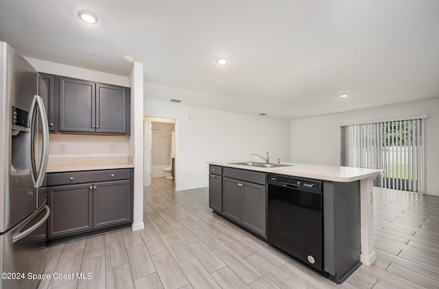 kitchen featuring black dishwasher, an island with sink, light hardwood / wood-style flooring, stainless steel fridge, and sink