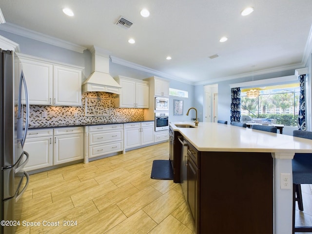 kitchen featuring premium range hood, appliances with stainless steel finishes, crown molding, and sink